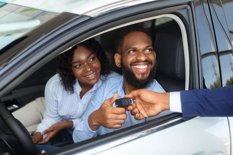 Happy African American Couple Taking Key From Salesman After Buying New Car